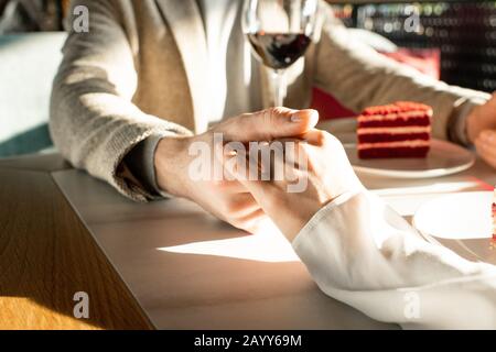 Uomo e donna irriconoscibili che amano passare il tempo in un ristorante moderno, delicatamente tenendo le mani, scatto orizzontale Foto Stock