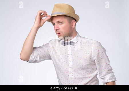 Allegro giovane uomo saluta prendendo un cappello. Studio girato su parete bianca. Foto Stock