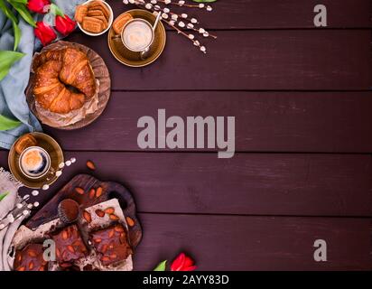 Colazione di Pasqua con caffè espresso fresco aromatico, croissant, torta brownie, uova colorate, tulipani rossi e salice. Caffè con dolci, fiori su un tavolo di legno. Vista dall'alto Foto Stock