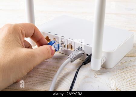 Donna collegare un cavo di rete blu alla presa di un router wireless Wi-Fi bianco su un tavolo bianco. Router WLAN con cavi Internet collegati. Foto Stock