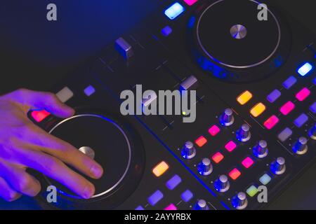 DJ riproduce musica. Controller mixer audio con manopole e cursori vicini. Mani sul mixer con giradischi al buio con comandi illuminati Foto Stock