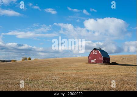 Nuvole sopra un campo di grano raccolto con un fienile rosso (Palouse Barn) nell'autunno vicino a Pullman nella Whitman County a Palouse, Washington state, USA. Foto Stock