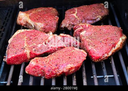 Bistecche crude condite su una griglia barbecue. Foto Stock