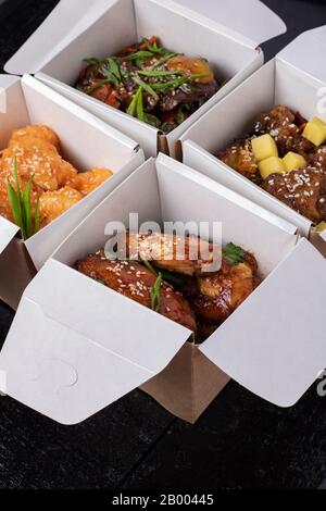 Piatti cinesi assortiti in scatole di consegna carta: Pollo dolce e acido, tagliatelle, insalata, riso, panini al vapore, salse. Disposizione piatta Foto Stock