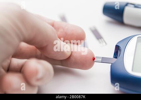 L'uomo prende il sangue dal dito usando la striscia di prova per controllare il livello di zucchero nel sangue con il glucometro. Concetto di diabete. Primo piano, messa a fuoco selettiva Foto Stock