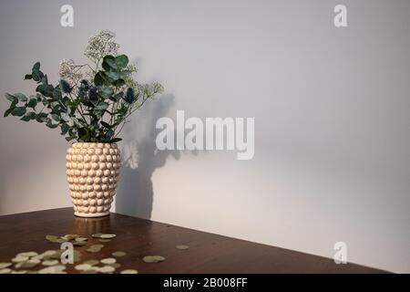 Vaso con un bouquet di fiori bianchi e blu su un tavolo di legno prima di uno sfondo grigio. Confetti dorati sdraiati sul tavolo. Foto Stock