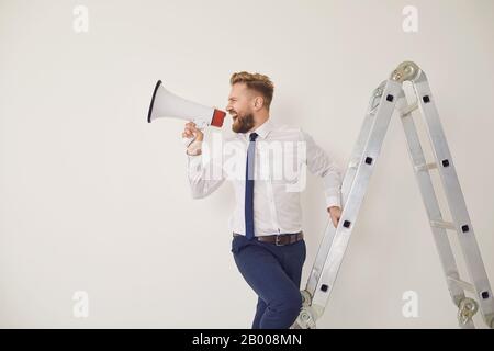 Un uomo d'affari barbuto sulle scale con un megafono in mano grida Foto Stock