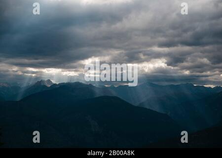 Luce del sole che passa attraverso le nuvole su molte montagne Foto Stock