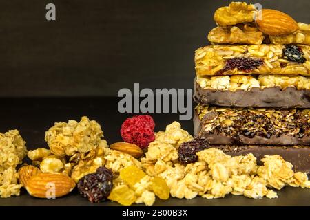 Barrette di granola con noci tostate, fuoco selettivo. Bar con farinata d'avena e noci su sfondo nero. Nutrizione per gli atleti. Dolcezza vegetariana. Foto Stock