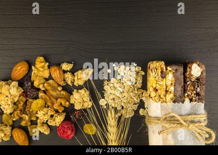 Barrette di granola con noci tostate, fuoco selettivo. Bar con farinata d'avena e noci su sfondo nero. Nutrizione per gli atleti. Dolcezza vegetariana. Foto Stock