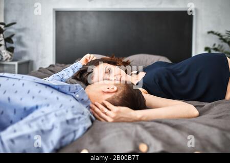 coppia incinta amorevole, sdraiati sul letto e guardarsi l'un l'altro. In attesa del bambino, una nuova vita, felicità e problemi di una giovane famiglia Foto Stock