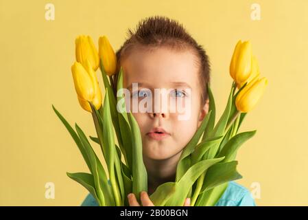 Carino ragazzino che tiene un bouquet di fiori. Tulipani. Festa Delle Madri. Giornata Internazionale Della Donna. Ritratto di un ragazzino felice su sfondo bianco. Sp Foto Stock