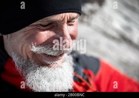 Ritratto di uomo runner anziano con barba grigia sorridente sullo sfondo della montagna invernale