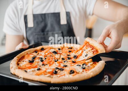 Primo piano italiano caldo fresco pizza margherita con olive in mani di chef maschile Foto Stock