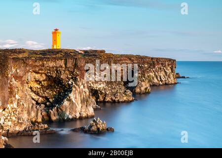 Faro arancione di Oendverdarnes sorge sulla costa della scogliera, costa rocciosa di roccia lavica, esposizione a lungo termine, Oendveroarnes, Snaefellsjoekull National Foto Stock