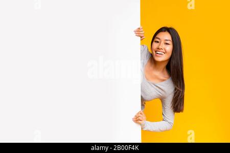 Bella ragazza asiatica guardando da dietro bordo bianco di pubblicità Foto Stock