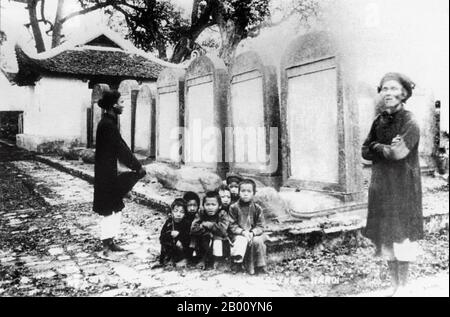 Vietnam: I bambini squat per una fotografia di fronte alle stele di pietra al Tempio della Letteratura, Hanoi (inizio 20 ° secolo). Anche se ci sono molti 'Templi della Letteratura" (Van Mieu) in Vietnam, questo ad Hanoi è di gran lunga il più conosciuto. Fu fondata nel 1070 come tempio confuciano e nel 1076 divenne la prima università del paese. L'Imperatore le Thanh Tong stabilì la tradizione, risalente al 1484, di intagliare i nomi dei vincitori dell'università su stele di pietra poste in cima a tartarughe di pietra. Foto Stock