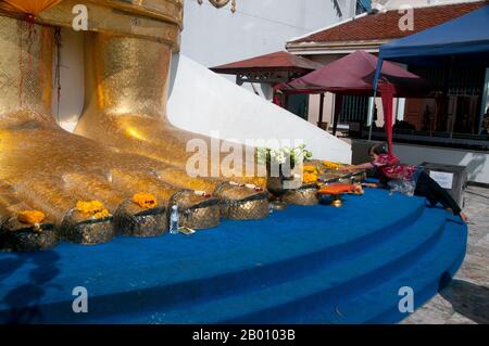 Thailandia: Un devoto mette i fiori ai piedi del gigante Buddha in piedi, Wat Intharawihan, Bangkok. La caratteristica principale del Wat Intharawihan di Bangkok è il Buddha alto 32 metri chiamato Luang Pho to o Phrasiariyametri. Ci sono voluti oltre 60 anni per essere completato ed è decorato in mosaici di vetro e oro di 24 carati. Il topnodo dell'immagine del Buddha contiene una reliquia del Buddha portato dallo Sri Lanka. Il tempio fu costruito all'inizio del periodo Ayutthaya. Foto Stock