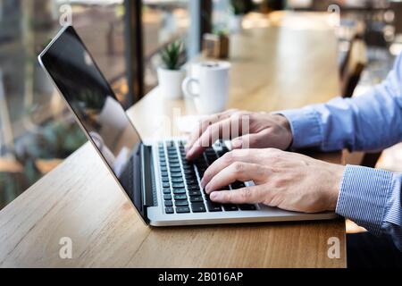 Mani che digitano sulla tastiera del computer portatile, persona che scrive e-mail o rapporto documento in caffè con caffè e internet wifi, stile casual, copia-spazio Foto Stock