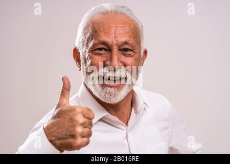 Ritratto di uomo anziano allegro che sta mostrando il pollice in su. Foto Stock