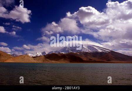 Cina: Muztagh ATA (Ice Mountain Padre) accanto al Lago Karakul sulla Karakoram Highway, Xinjiang. Muztagh ATA, o Muztagata (Uyghur: 'Padre di montagna di ghiaccio'), è il secondo più alto (7546 metri) delle montagne che formano il bordo settentrionale dell'altopiano tibetano (non il secondo più alto delle montagne dell'altopiano tibetano). A volte è considerato come parte del Kunlun Shan, anche se fisicamente è più strettamente collegato ai Pamirs. Si presume inoltre che sia una delle vette più facili da scalare di 7.000 m del mondo, a causa del suo dolce pendio occidentale e del tempo relativamente più secco. Foto Stock