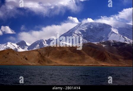 Cina: Muztagh ATA (Ice Mountain Padre) accanto al Lago Karakul sulla Karakoram Highway, Xinjiang. Muztagh ATA, o Muztagata (Uyghur: 'Padre di montagna di ghiaccio'), è il secondo più alto (7546 metri) delle montagne che formano il bordo settentrionale dell'altopiano tibetano (non il secondo più alto delle montagne dell'altopiano tibetano). A volte è considerato come parte del Kunlun Shan, anche se fisicamente è più strettamente collegato ai Pamirs. Si presume inoltre che sia una delle vette più facili da scalare di 7.000 m del mondo, a causa del suo dolce pendio occidentale e del tempo relativamente più secco. Foto Stock