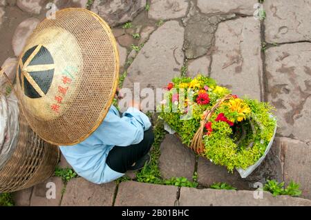 Cina: Donna Tujia che vende tiaras di fiori alla Torre porta Nord, Fenghuang, Provincia di Hunan. Fenghuang è cinese per Phoenix e si riferisce al mitico uccello da fuoco sacro che si può trovare nelle mitologie dei Persiani, Greci, Romani, Egiziani, Cinesi, E (secondo Sanchuniathon) i Fenici. La leggenda suggerisce che due phoenixes sulla scoperta della città hovered sopra per un certo tempo considerevole prima di volare riluttante via. Fenghuang è un'antica città ben conservata che risale al 248 a.C. Ospita le minoranze Miao e Tujia. Foto Stock