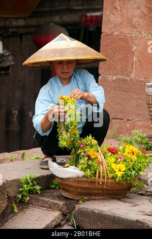 Cina: Donna Tujia che vende tiaras di fiori alla Torre porta Nord, Fenghuang, Provincia di Hunan. Fenghuang è cinese per Phoenix e si riferisce al mitico uccello da fuoco sacro che si può trovare nelle mitologie dei Persiani, Greci, Romani, Egiziani, Cinesi, E (secondo Sanchuniathon) i Fenici. La leggenda suggerisce che due phoenixes sulla scoperta della città hovered sopra per un certo tempo considerevole prima di volare riluttante via. Fenghuang è un'antica città ben conservata che risale al 248 a.C. Ospita le minoranze Miao e Tujia. Foto Stock