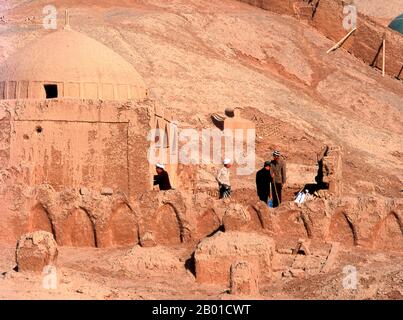 Cina: Uomini che lavorano su una tomba nel cimitero vicino al villaggio di Tuyoq vicino Turpan, provincia di Xinjiang. Tuyoq o Tuyugou è un'antica oasi-villaggio nel deserto di Taklamakan, 70 km a est di Turpan in una valle lussureggiante che si estende nelle Flaming Mountains, con un ben conservato orientamento Uyghur. E' famosa per le sue uve senza semi e per un certo numero di antiche grotte di meditazione buddista nelle vicinanze contenenti affreschi, la piu' conosciuta essendo le Grotte dei Mille Buddha di Bezeklik. Foto Stock