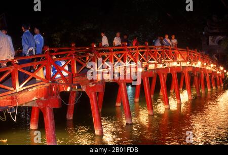 Vietnam: Il rosso dipinto il ponte Huc (Rising Sun o Sunbeam Bridge) che conduce a Den Ngoc Son o Jade Mountain Temple, lago Hoan Kiem, Hanoi. Ho Hoan Kiem significa “Lago della spada restaurata”, un corpo d’acqua che si trova nel cuore di Hanoi. Fino al 15th ° secolo fu chiamato Luc Thuy o 'acqua verde'. La leggenda vuole che durante l'occupazione di Ming (1407-28), il generale le Loi fu presentato con una spada magica da una tartaruga divina che viveva nelle acque. Con l'aiuto di questa spada, le Loi espulse i cinesi dal nord del Vietnam e si stabilì come imperatore le Thai a. Foto Stock