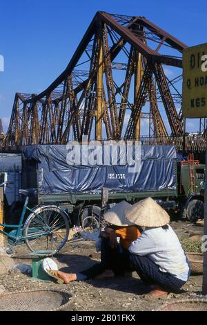 Vietnam: Donne vicino al ponte Long Bien, Hanoi. Il ponte Long Bien fu eretto dai colonialisti francesi tra il 1899 e il 1902 e nominato ponte Paul Doumer in onore dell'allora governatore dell'Indochina francese (1897-1902). È stato progettato e costruito da Dayde e Pille di Parigi (le placche originali sono ancora in atto) ed è lungo 1.682 metri (5.518 piedi), composto da 18 campate, con un'ulteriore estensione centrale allungata di 106 metri (347 piedi). Trasporta l'unica linea ferroviaria tra Hanoi e Haiphong, così come due collegamenti ferroviari vitali con la Cina. Foto Stock