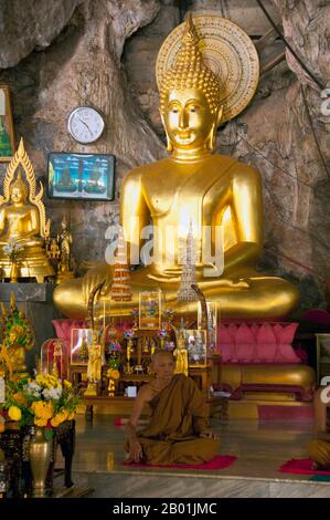 Thailandia: Monk and Buddha, Wat Tham Seua, Krabi Town, Krabi Province, Thailandia meridionale. Wat Tham Seua, il "Tempio della Grotta della Tigre" è costruito in una grotta posta su una scogliera calcarea. Circondato da residenze individuali dei monaci, questo è uno dei templi forestali più noti della Thailandia meridionale. Il viharn principale o sala delle assemblee si estende in una lunga e poco profonda grotta calcarea che mostra vari oscuri ricordi della mortalità come contrappeso ai desideri mondani. Sul retro della grotta una rampa di scale di marmo conduce alla "grotta della tigre" stessa. Foto Stock