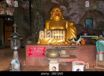 Thailandia: Laughing Buddha, Wat Tham Seua, Krabi Town, Krabi Province, Thailandia meridionale. Wat Tham Seua, il "Tempio della Grotta della Tigre" è costruito in una grotta posta su una scogliera calcarea. Circondato da residenze monache individuali, questo è uno dei templi forestali più noti della Thailandia meridionale. Il viharn principale o sala di assemblaggio si estende in una lunga grotta calcarea poco profonda che mostra vari tristi ricordi della mortalità come controbilanciamento ai desideri mondani. Sul retro della grotta una rampa di scale di marmo conduce alla "grotta della tigre" stessa. Foto Stock