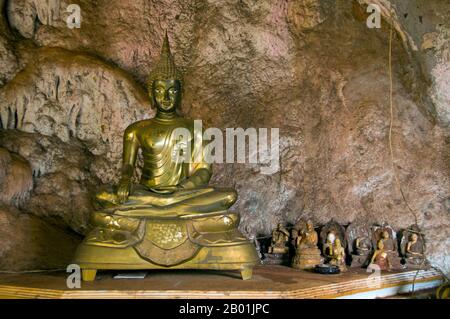 Thailandia: Buddha, Wat Tham Seua, Krabi Town, provincia di Krabi, Thailandia meridionale. Wat Tham Seua, il "Tempio della Grotta della Tigre" è costruito in una grotta posta su una scogliera calcarea. Circondato da residenze monache individuali, questo è uno dei templi forestali più noti della Thailandia meridionale. Il viharn principale o sala di assemblaggio si estende in una lunga grotta calcarea poco profonda che mostra vari tristi ricordi della mortalità come controbilanciamento ai desideri mondani. Sul retro della grotta una rampa di scale di marmo conduce alla "grotta della tigre" stessa. All'interno c'è una venerata impronta di Buddha su una piattaforma dorata. Foto Stock