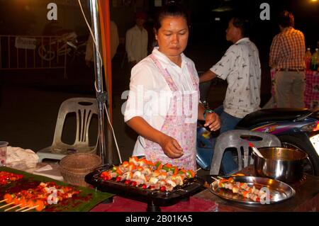 Thailandia: Venditore di kebab al mercato domenicale accanto alla stazione ferroviaria, Trang Town, Trang Province, Thailandia meridionale. Trang è stato un centro commerciale almeno dal i secolo d.C. Crebbe fino alla prosperità tra il VII e il XIII secolo durante il periodo Srivijaya e rimane oggi un'importante città commerciale. Gomma, olio di palma e pesca sono i pilastri dell'economia cittadina. Il turismo sta avendo un impatto crescente poiché la costa delle Andamane e le isole di Trang sono sempre più sviluppate e diffuse. Foto Stock