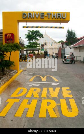 Filippine: St William's Cathedral vista da un McDonald's Drive Thru, Laoag, Ilocos Norte, Luzon Island. St La Cattedrale di Guglielmo, nota anche come Cattedrale di Laoag, fu originariamente costruita nel 1612 dai frati agostiniani per sostituire una cappella di legno. È noto per il suo design rinascimentale italiano e per il suo campanile che affonda nel terreno ad un ritmo di un pollice all'anno. Laoag (Ilocano per "luce o chiarezza"), è un antico e fiorente insediamento conosciuto dai commercianti cinesi e giapponesi quando il conquistador spagnolo Juan de Salcedo arrivò sulle rive settentrionali del fiume Padsan nel 1572. Foto Stock