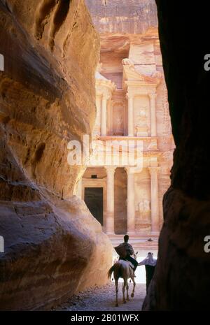 Giordania: The Siq (Shaft) e al Khazneh (The Treasury) in background, Petra. Il Siq o al-Siq ("il pozzo") è l'ingresso principale dell'antica città di Petra nel sud della Giordania. La dim e stretta gola (in alcuni punti non più di 3 metri di larghezza) si snoda per circa un miglio e termina alla rovina più elaborata di Petra, al Khazneh (il Tesoro). Petra fu fondata come città dagli arabi nabatei nel IV secolo a.C. e doveva la sua nascita e prosperità al fatto che era l'unico luogo con acqua chiara e abbondante tra i centri commerciali Hijaz della Mecca e Medina. Foto Stock