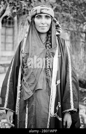 Giordania: Una donna beduina che indossa un abito ricamato, Wadi Musa, Petra, 1900 I beduini fanno parte di un gruppo etnico arabo che abita prevalentemente nel deserto tradizionalmente diviso in tribù o clan, conosciuto in arabo come ʿašāʾir. Per "beduini" si intendono "quelli di bādiyah" o "quelli del deserto". A partire dalla fine del XIX secolo, molti beduini sotto il dominio britannico iniziarono a transitare verso una vita semi-nomade. Negli anni '1950 e '1960, un gran numero di beduini in tutto il Midwest Asia iniziò a lasciare la tradizionale vita nomade per stabilirsi nelle città. Foto Stock