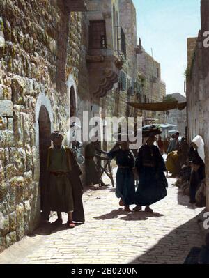 Palestina: Palestinesi nella strada che conduce alla Chiesa della Natività a Betlemme, 1898-1919. Palestina è un nome dato alla regione geografica tra il Mar Mediterraneo e il fiume Giordano. La regione è anche conosciuta come la Terra di Israele (Eretz-Yisra'el), la Terra Santa e il Levante meridionale. Nel 1832 la Palestina fu conquistata dall'Egitto di Muhammad Ali, ma nel 1840 la Gran Bretagna intervenne e restituì il controllo del Levante agli ottomani in cambio di ulteriori capitolazioni. La fine del XIX secolo vide l'inizio dell'immigrazione sionista e la rinascita della lingua ebraica. Foto Stock