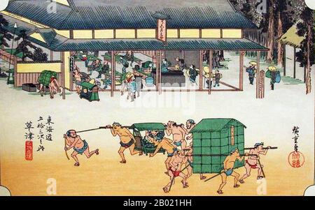 Giappone: "Stazione 52: Kusatsu, Una stazione famosa per le sue torte di riso". Ukiyo-e xilografia della serie '53 stazioni della strada Tôkaidô' di Utagawa Hiroshige (1797-1858), 1834 circa. Kusatsu: Vista di una casa di riposo per raffreddori e cavalli sulla strada; coolie che passano in primo piano con un kago e un palanchino coperto. La Nakasendo, un'altra grande autostrada che correva attraverso la regione montuosa tra Edo e Kyoto, si unì al Tokaido in questa stazione per formare un'unica autostrada per il resto dell'autostrada per Kyoto. Foto Stock