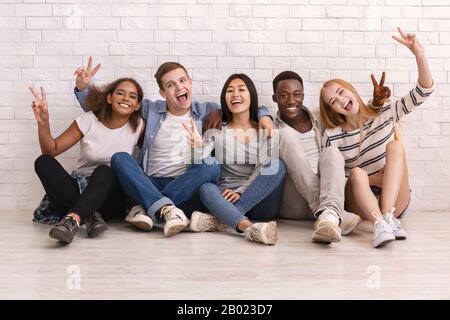 Studenti multirazziali emotivi seduti a terra e in posa alla macchina fotografica Foto Stock