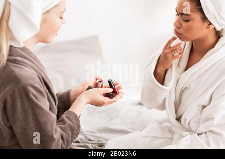 Ragazza nera pensierosa in accappatoio scelta del colore della lucidatrice del chiodo Foto Stock