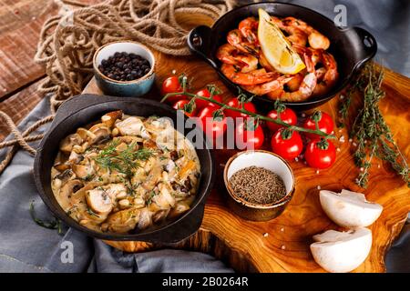 Gran fritto di gamberi in salsa di pomodoro con olio di oliva,funghi in salsa di panna julienne, champignon, prodotti per la cottura sul tavolo di legno sfondo Foto Stock