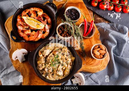 Gran fritto di gamberi in salsa di pomodoro con olio di oliva,funghi in salsa di panna julienne, champignon, prodotti per la cottura sul tavolo di legno sfondo Foto Stock