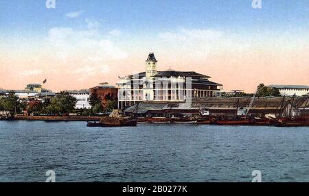 Tanzania/Zanzibar: Barche al lungomare godown, palazzo e Beit al-Ajaib sullo sfondo, 1910 circa. Zanzibar è una parte semi-autonoma della Tanzania nell'Africa orientale. È composto dall'arcipelago di Zanzibar nell'Oceano Indiano, 25-50 km (16-31 miglia) al largo della costa continentale, ed è costituito da numerose piccole isole e due grandi: Unguja (l'isola principale, indicata informalmente come Zanzibar), e Pemba. La capitale di Zanzibar, situata sull'isola di Unguja, è Zanzibar City. Il suo centro storico, conosciuto come Stone Town, è un sito Patrimonio dell'Umanità. Foto Stock