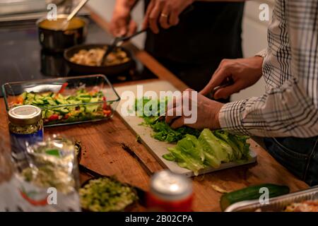 2 uomo che fa la cena che prepara l'insalata di cibo per i loro wifes per la festa della donna Foto Stock