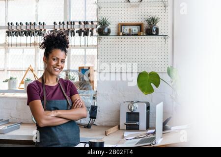 Donna sorridente in piedi da un banco di lavoro nel suo negozio di cornice Foto Stock