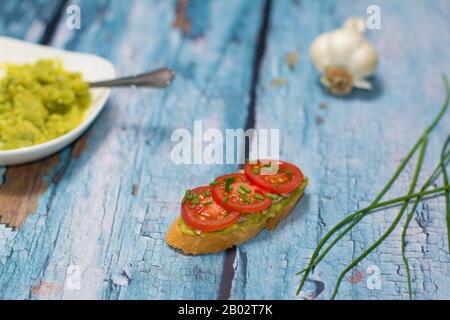 Un panino a vista fatto di baguette, avocado spalmato, fette di pomodoro ciliegia, e erba cipollina tagliata a dadini, erba cipollina verde sono visibili accanto ad esso. Foto Stock