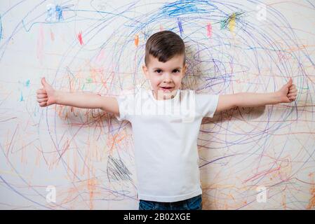 Il bambino è impegnato nella creatività a casa. Il ragazzo si posa sullo sfondo del muro dipinto da lui Foto Stock