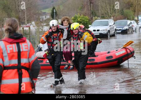 Una donna è sollevata alla sicurezza dai soccorritori come acqua di inondazione circonda il villaggio di Whitchurch in Herefordshire, dopo che il fiume Wye ha scoppiato le sue banche nel periodo successivo alla tempesta Dennis. Foto Stock